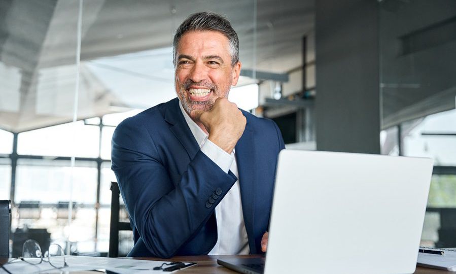 Happy middle aged business man ceo working on laptop laughing in office.